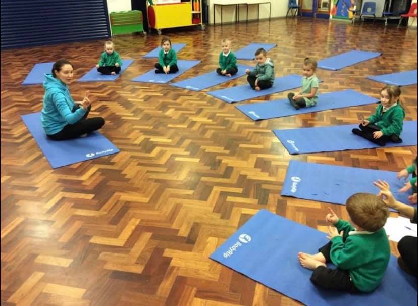 Primary school yoga class with kids sat on their mats listening to the yoga teacher
